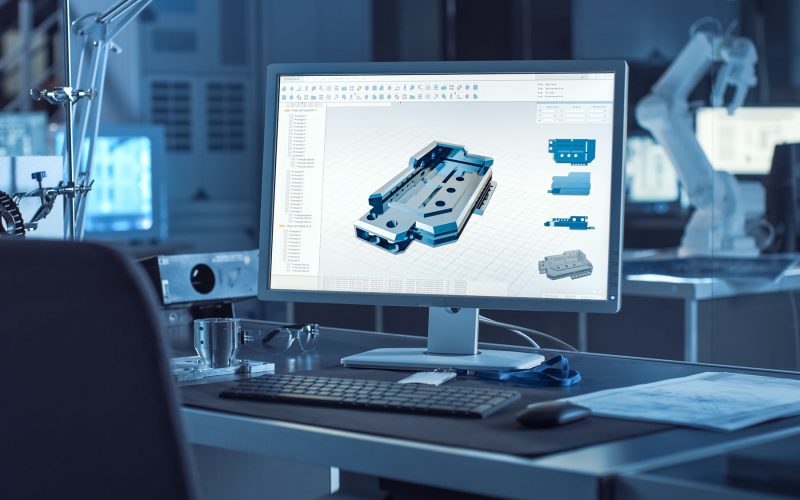 On the Desk Computer With CAD Software and Design of 3D Industrial Machinery Component. In the Background Robot Arm Concept Standing in Heavy the Dark.Industry Engineering Facility.