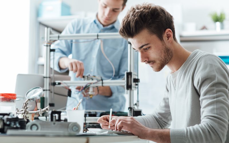 Engineering students working in the lab, a student is using a 3D printer in the background